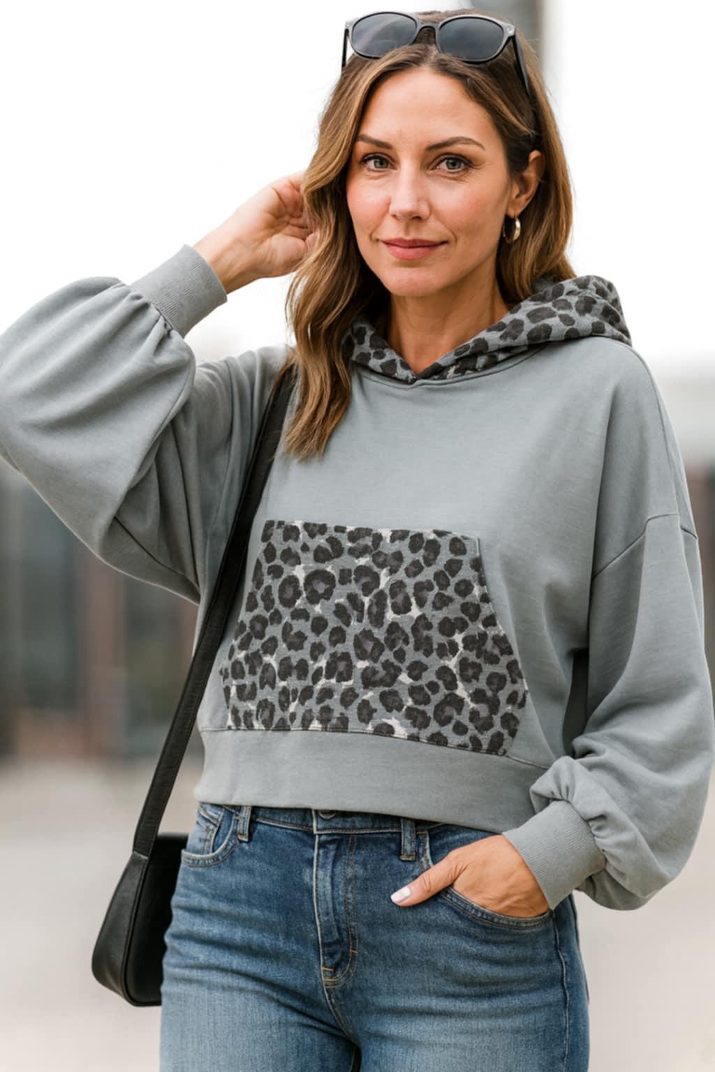 . Urban chic woman wearing a gray hoodie with leopard print pocket and hood, styled with jeans.