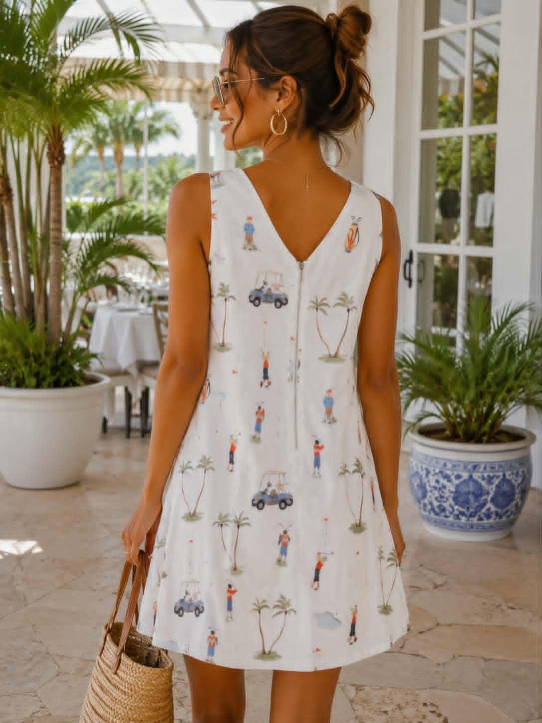 A woman wearing a sleeveless white V-neck dress with a colorful golf-themed print, standing on a patio and holding a straw bag.