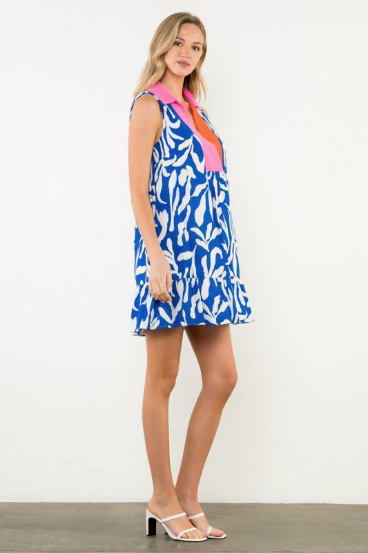 Woman wearing a blue patterned dress with pink and orange accents on a white background