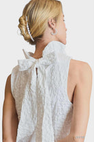 Back view of white sleeveless dress featuring an oversized bow at the neckline.