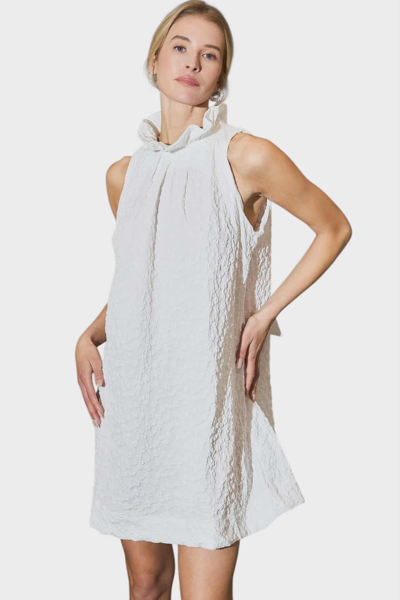 Woman wearing a white sleeveless dress with lace details on a white background