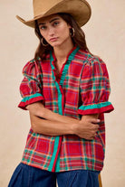 Woman wearing red plaid blouse with green trim and ruffled puff sleeves – festive holiday top by Petunias of Naples
