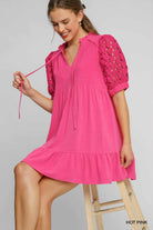 Woman wearing a bright pink dress with cut-out sleeves on a gray background