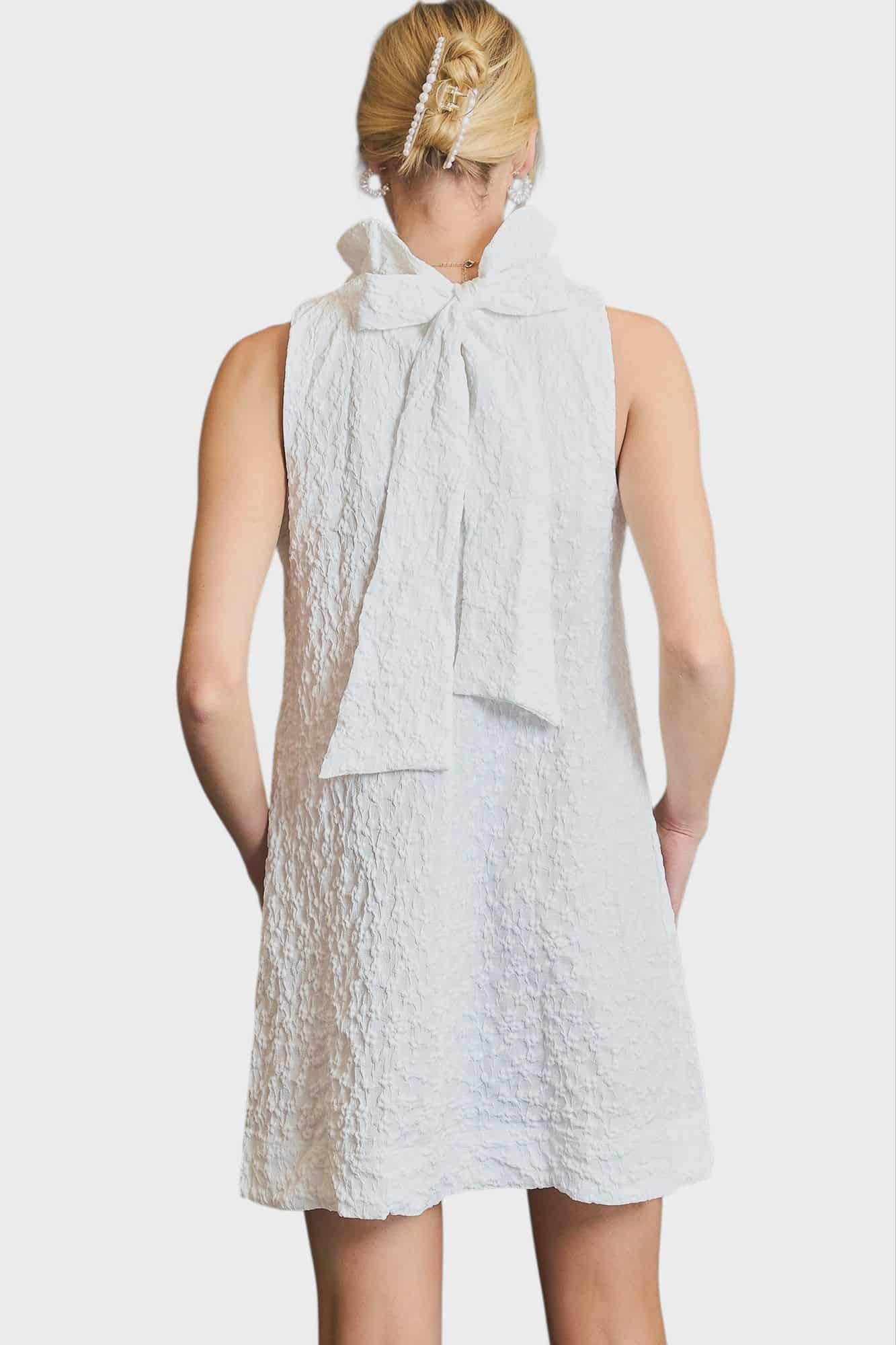 Back view of white sleeveless dress featuring an oversized bow at the neckline.