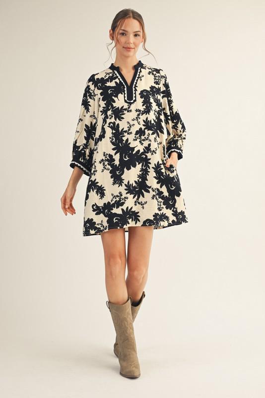 Model wearing Jodifl black and cream floral tunic dress with scalloped trim neckline and ¾ sleeves, photographed against white background— Petunias of Naples