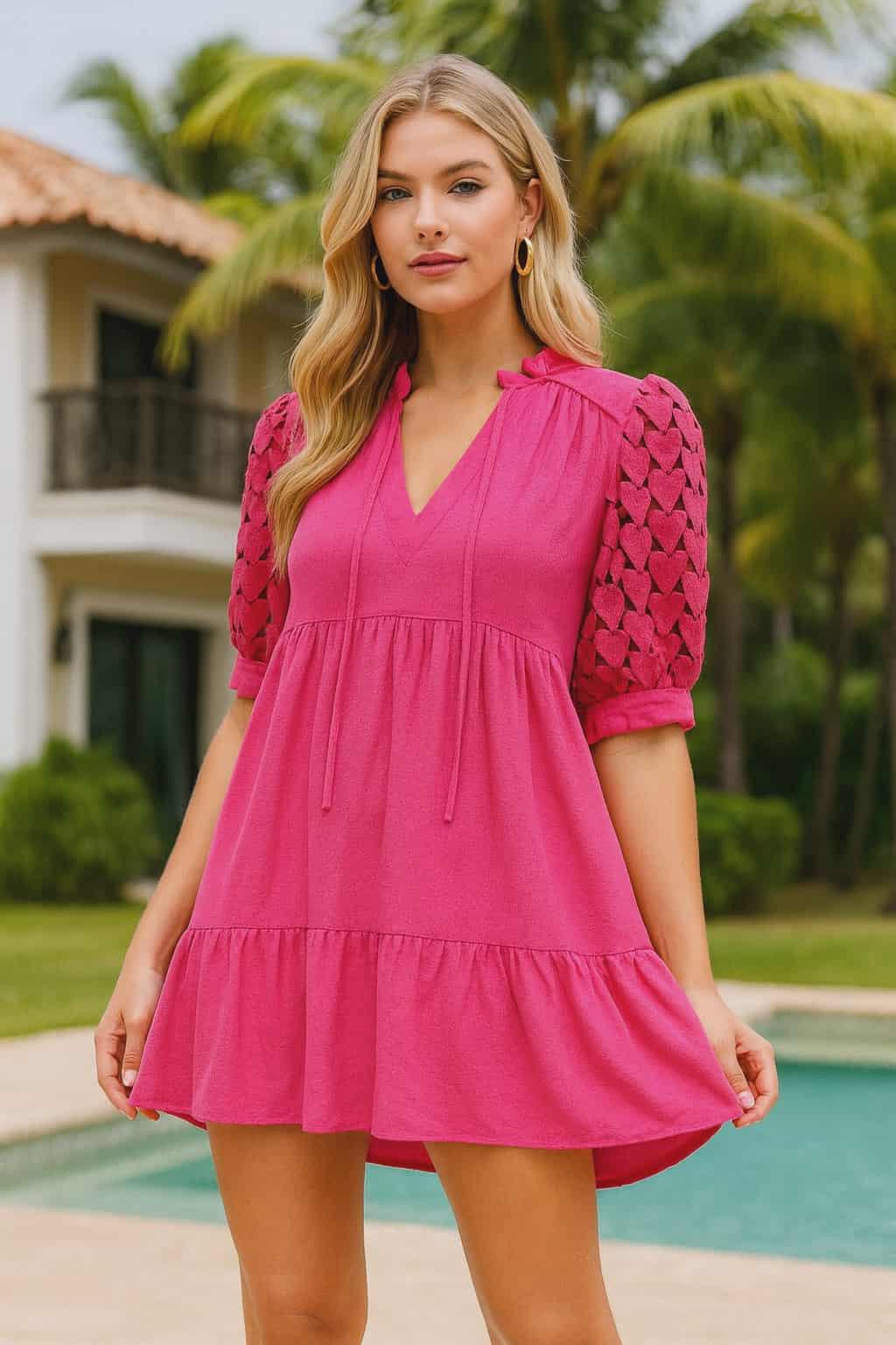 Resort chic woman wearing a hot pink linen blend babydoll dress with crochet puff sleeves, posing by a tropical pool.