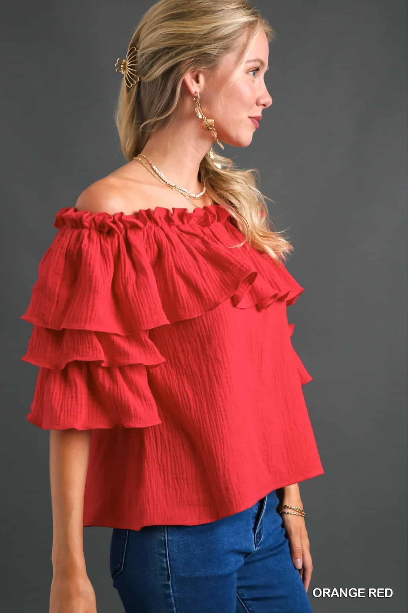 Woman wearing a red off-shoulder ruffled top against a gray background, side view