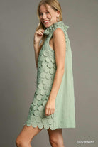 Woman wearing a light green dress with a textured pattern on a gray , side viewbackground
