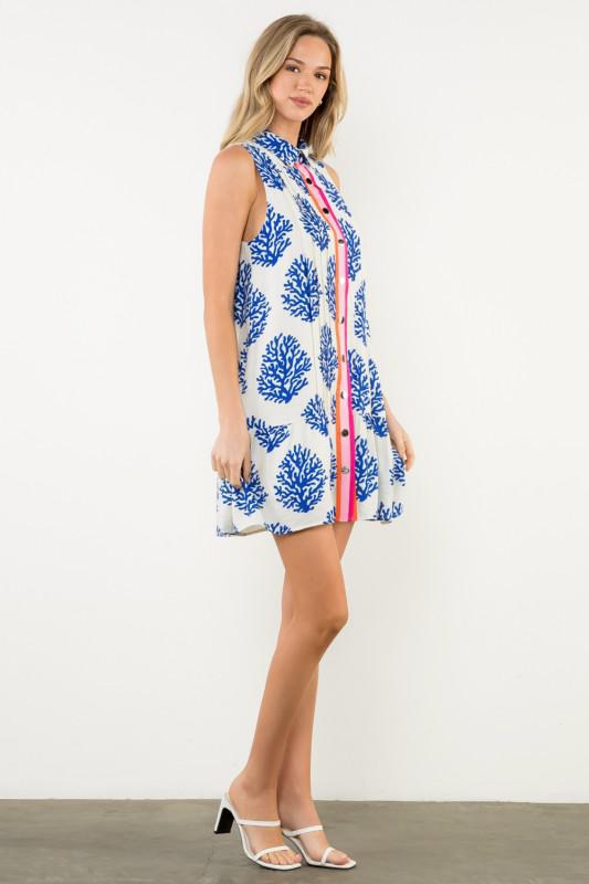 Woman wearing a sleeveless dress with a blue floral pattern on a white background, sideview