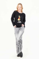 Model wearing Gabby Isabella black sweater featuring a colorful fashion-girl graphic with a yellow coat and red handbag,  WHITE BACKGROUND— Petunias of Naples